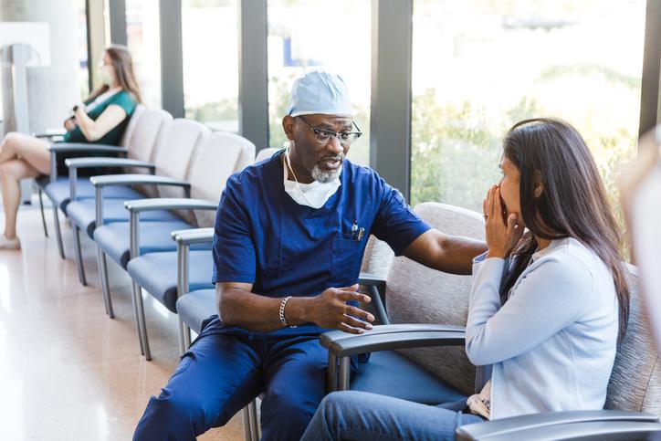 The doctor places his hands on the female patient's shoulder as he gives some bad news about the test results.