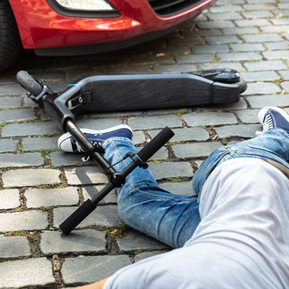 E-Scooter on the ground next to a car, symbolizing an accident E-Scooter on the ground next to a car, symbolizing an accident
