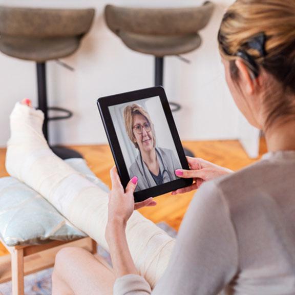 Young adult woman with cochlear implant, using digital tablet for conversation with her doctor. She is sitting on the chair in the living room and has video call and consultation with her female doctor.
