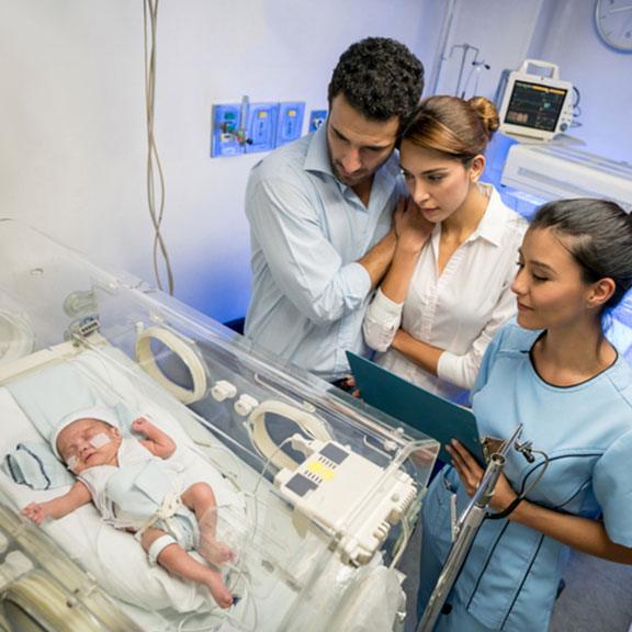 Young couple looking at their new born baby in an incubator with oxygen looking very concerned and partner embracing woman while nurse standing next to them. Young couple looking at their new born baby in an incubator with oxygen looking very concerned and partner embracing woman while nurse standing next to them.